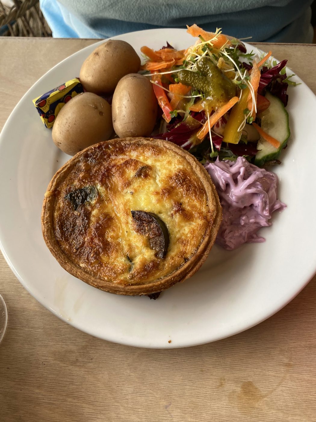 A slice of quiche with new potatoes and salad
